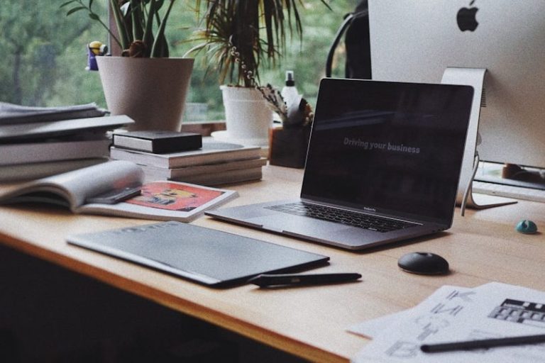 Ein moderner Schreibtisch mit Laptop, Tablet, Notizen und Pflanzen im Hintergrund.