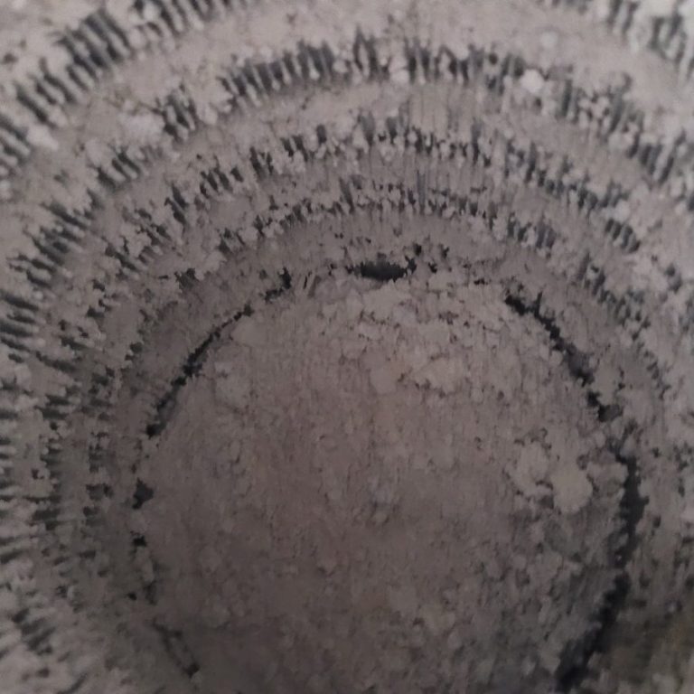 Blick in einen zylindrischen Behälter mit grauem, pulvrigem Inhalt.