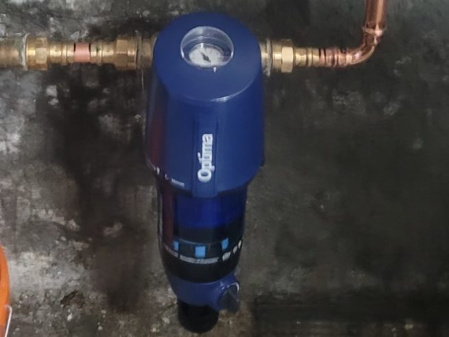 Blauer Wasserfilter mit Druckanzeige und Kupferrohren.